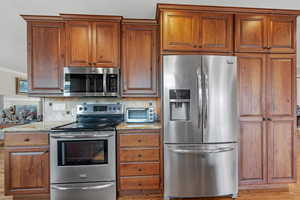 Kitchen featuring light stone counters, a toaster, crown molding, stainless steel appliances, and backsplash