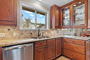 Kitchen featuring light stone counters, stainless steel dishwasher, a sink, and glass insert cabinets