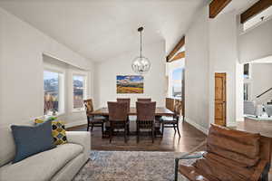 Dining space featuring beam ceiling, an inviting chandelier, dark wood-type flooring, high vaulted ceiling, and baseboards