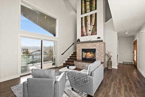 Living area with a stone fireplace, a high ceiling, visible vents, baseboards, and dark wood finished floors