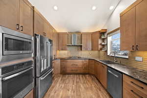 Kitchen with open shelves, decorative backsplash, appliances with stainless steel finishes, a sink, and wall chimney range hood