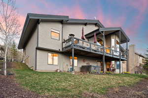 Back of property at dusk featuring a yard, a hot tub, and a wooden deck