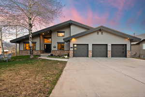 View of front facade featuring a garage, concrete driveway, a yard, and stone siding