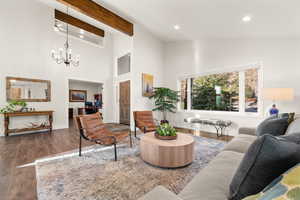 Living room featuring dark wood-type flooring, an inviting chandelier, high vaulted ceiling, beam ceiling, and recessed lighting