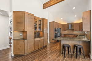 Kitchen featuring wall chimney exhaust hood, glass insert cabinets, a breakfast bar, stainless steel appliances, and a sink