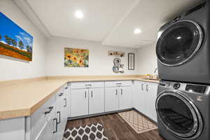 Washroom featuring recessed lighting, dark wood-type flooring, stacked washer / dryer, a sink, and cabinet space