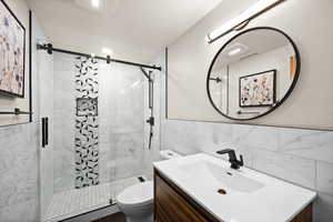 Full bathroom featuring a stall shower, visible vents, toilet, vanity, and tile walls