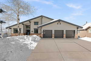 View of front facade featuring a garage, stone siding, a balcony, and concrete driveway