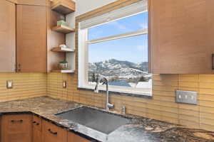 Kitchen featuring brown cabinetry, dark stone countertops, a mountain view, open shelves, and a sink