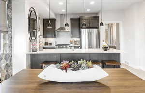 Kitchen featuring high quality fridge, light countertops, wall chimney range hood, hanging light fixtures, and range