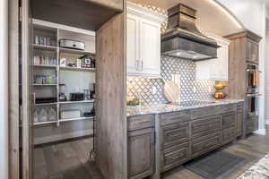 Kitchen featuring light stone counters, dark wood-style flooring, black electric stovetop, custom exhaust hood, and dark brown cabinets