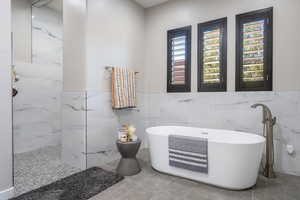 Bathroom with a freestanding tub, tile patterned flooring, a walk in shower, and a wainscoted wall