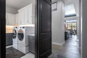 Laundry room with cabinet space, a barn door, baseboards, wood finished floors, and washing machine and clothes dryer