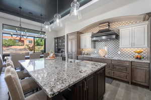 Kitchen featuring a breakfast bar, custom range hood, backsplash, dark brown cabinetry, and a large island with sink