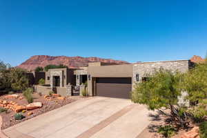 Pueblo-style house with a garage, concrete driveway, stone siding, a mountain view, and stucco siding