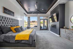 Bedroom featuring carpet, a tray ceiling, a glass covered fireplace, access to outside, and baseboards