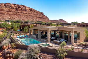 Rear view of property featuring a patio, a mountain view, an in ground hot tub, stucco siding, and an outdoor living space with a fireplace