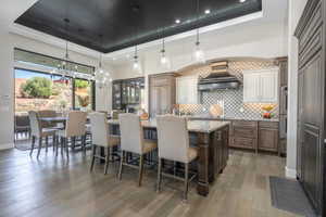 Kitchen with premium range hood, a kitchen bar, a raised ceiling, and a center island with sink