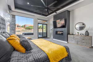 Bedroom featuring baseboards, a glass covered fireplace, access to exterior, a tray ceiling, and carpet flooring