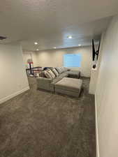 Unfurnished living room featuring baseboards, dark carpet, a textured ceiling, and recessed lighting