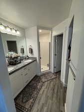 Bathroom with double vanity, a stall shower, wood finished floors, a textured ceiling, and a sink