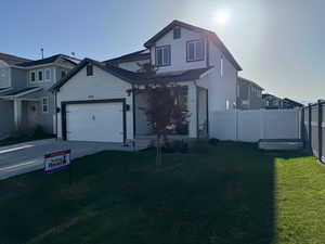 Traditional-style house featuring an attached garage, driveway, a front lawn, and fence