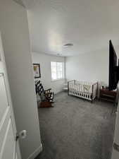 Bedroom with a textured ceiling, a nursery area, dark carpet, and baseboards