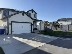 View of front facade featuring driveway, an attached garage, fence, a front yard, and a residential view