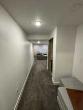 Corridor featuring a textured ceiling, dark carpet, and baseboards