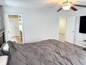 Bedroom featuring a ceiling fan, a glass covered fireplace, light carpet, and baseboards