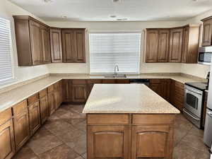 Kitchen with appliances with stainless steel finishes, light countertops, a sink, and a kitchen island