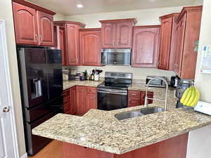 Kitchen featuring stainless steel appliances, a peninsula, dark brown cabinets, and light stone countertops