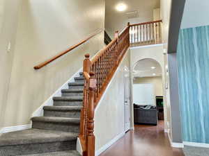 Stairway featuring arched walkways, a high ceiling, baseboards, and wood finished floors