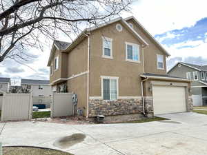 Exterior space with stone siding, fence, concrete driveway, and stucco siding