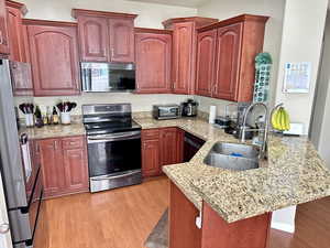 Kitchen with light wood-type flooring, reddish brown cabinets, appliances with stainless steel finishes, and a sink