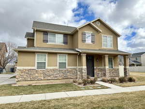 View of front of property with a porch, stone siding, roof with shingles, stucco siding, and a front yard