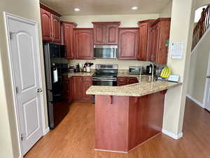 Kitchen with a peninsula, light wood finished floors, stainless steel appliances, and a kitchen breakfast bar