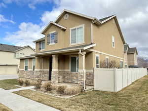 View of front of home featuring stone siding, a front yard, fence, and stucco siding