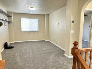 Carpeted spare room with arched walkways, a textured ceiling, visible vents, and baseboards