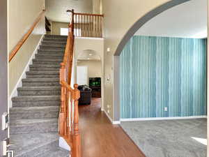 Stairway featuring arched walkways, a high ceiling, baseboards, and wood finished floors