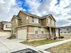 Townhome / multi-family property featuring an attached garage, stone siding, driveway, and stucco siding