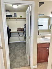 Walk in closet with light carpet, light tile patterned floors, and a sink