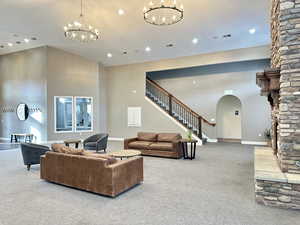 Living room with stairway, arched walkways, a notable chandelier, and carpet flooring