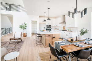 Kitchen with light countertops, hanging light fixtures, a kitchen island with sink, white cabinetry, and wall chimney exhaust hood