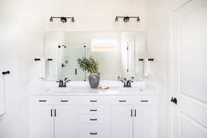 Bathroom featuring a sink, a shower stall, and double vanity