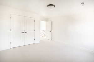 Unfurnished bedroom featuring a closet, light carpet, visible vents, and baseboards