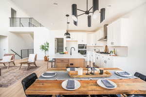 Kitchen featuring wall chimney exhaust hood, light countertops, a center island with sink, and white cabinets