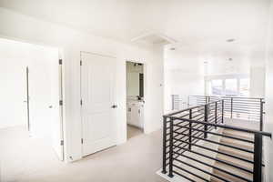 Hallway featuring light carpet, an upstairs landing, and attic access