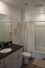 Full bathroom featuring visible vents, toilet, wood finished floors, shower / bathtub combination with curtain, and vanity