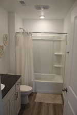 Bathroom featuring visible vents, toilet, shower / tub combo with curtain, wood finished floors, and vanity